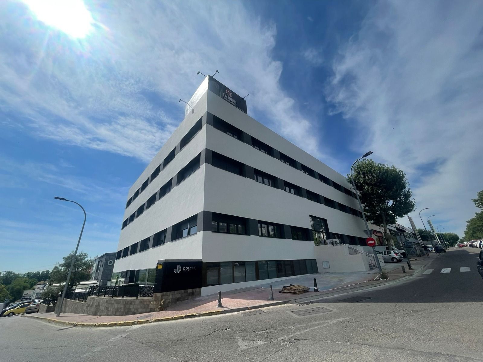 Edificio de oficinas moderno de color blanco con detalles negros, autos estacionados en la calle, día soleado.