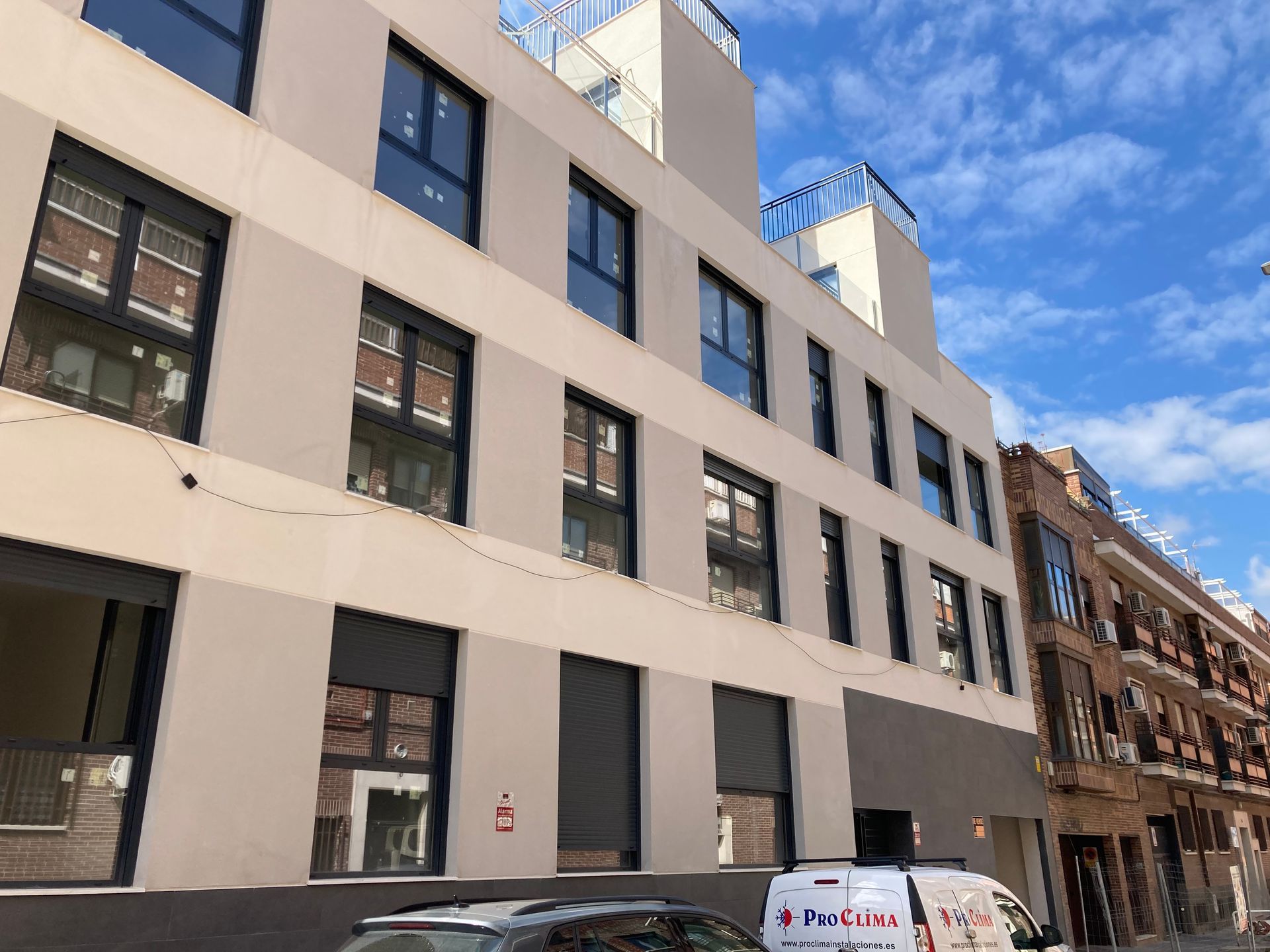 Edificio de varios pisos de color beige y negro con ventanas de marco oscuro bajo un cielo azul.