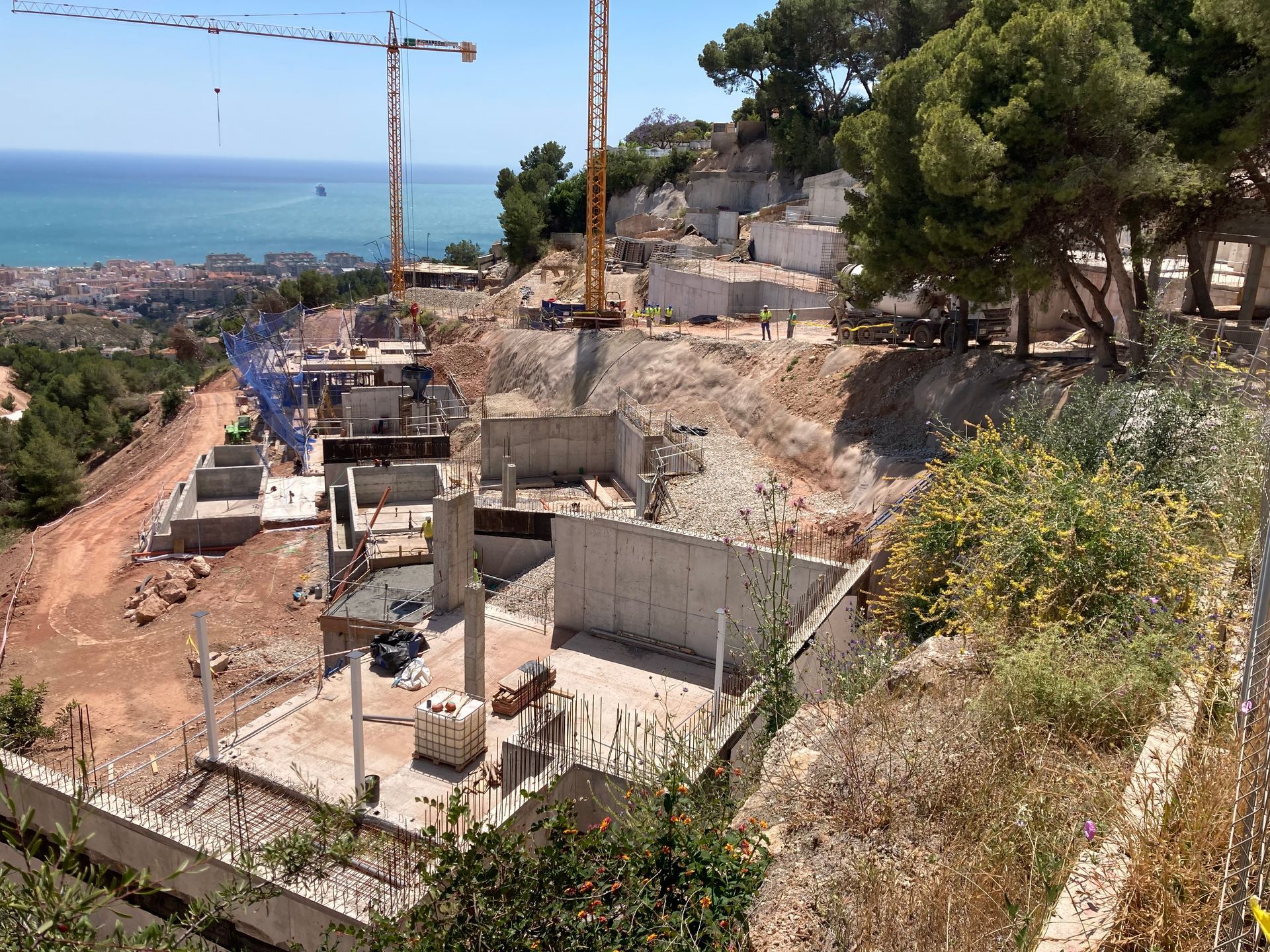 Obra en una ladera con vistas al océano. Estructuras de cemento, grúas y tierra expuesta.