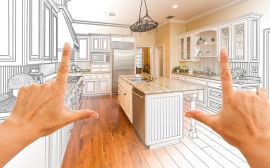 Bright kitchen with white cabinets and island, viewed through a hand framing gesture