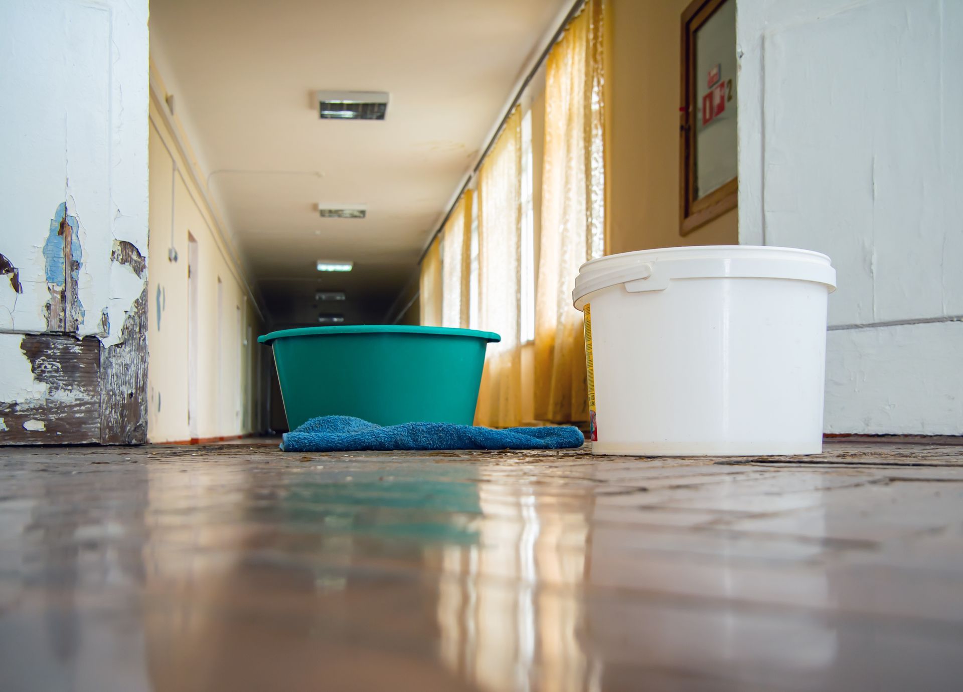 Water damage restoration with buckets collecting leaks on the flooded hallway floor.