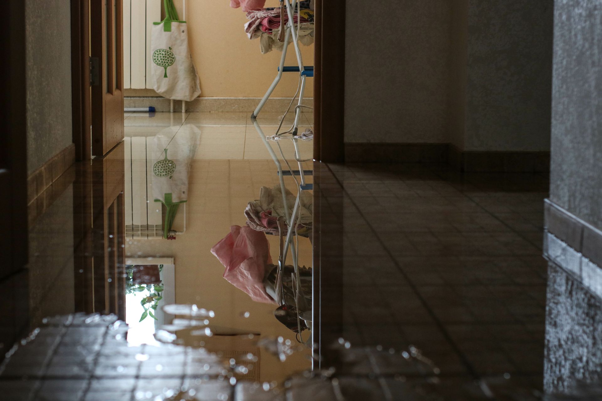 Indoor room flooded with water, reflecting objects like a drying rack and partially opened doors. Indoor room flooded with water, reflecting objects like a drying rack and partially opened doors.