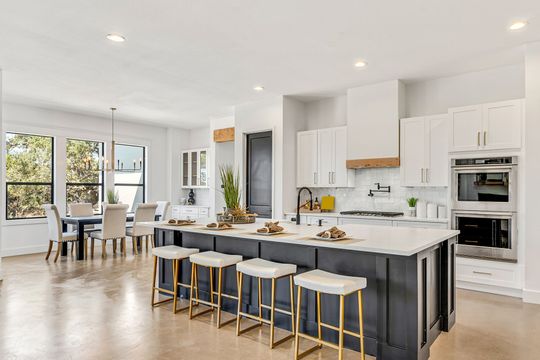 Modern white kitchen with large island, gold stools, and open dining area with windows and natural light