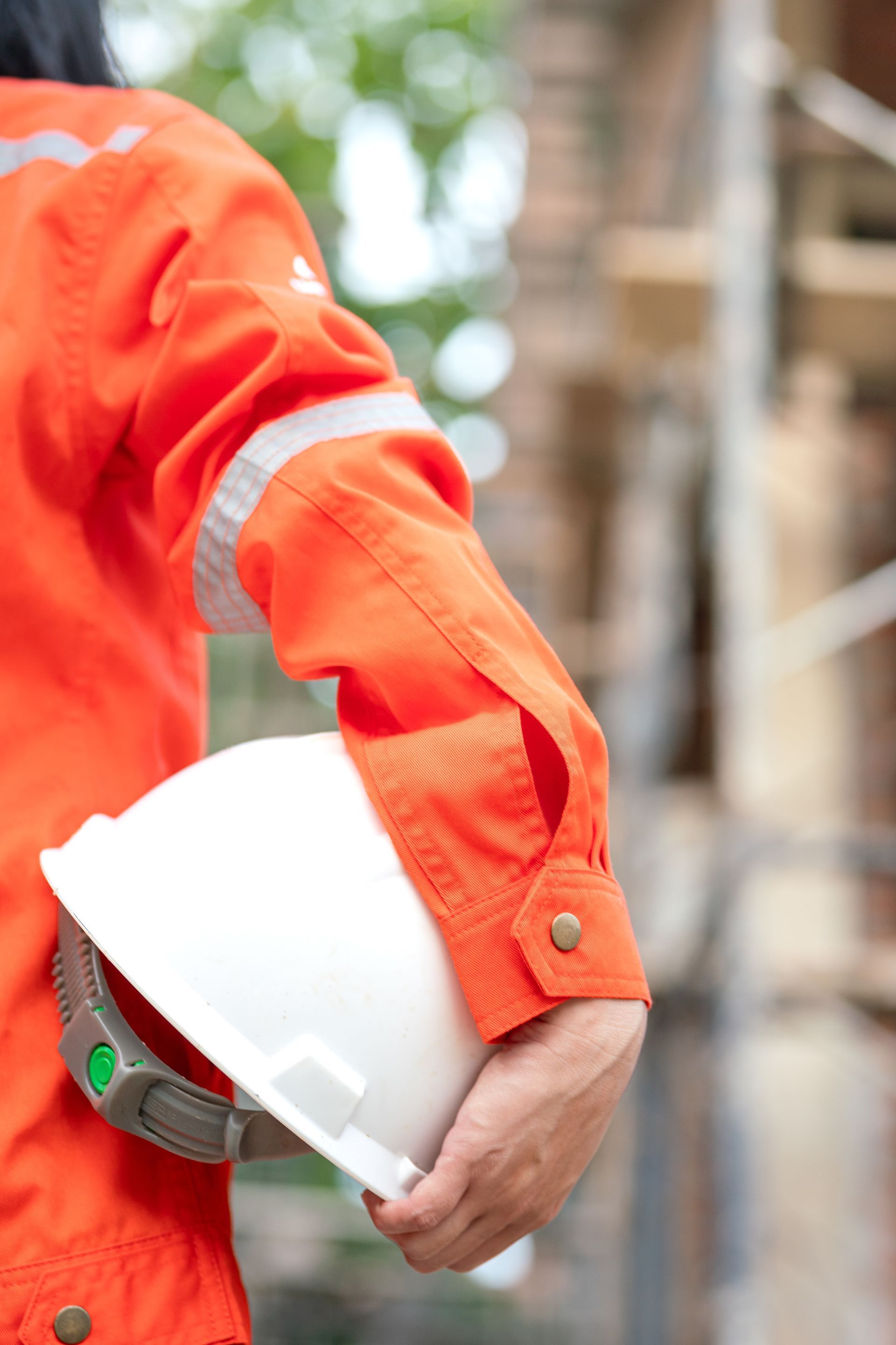 Construction worker in orange jumpsuit holding a white hard hat; construction site background. Construction worker in orange jumpsuit holding a white hard hat; construction site background.