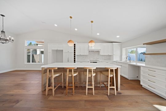 Bright modern kitchen with white cabinets, large island, wooden stools, and pendant lights
