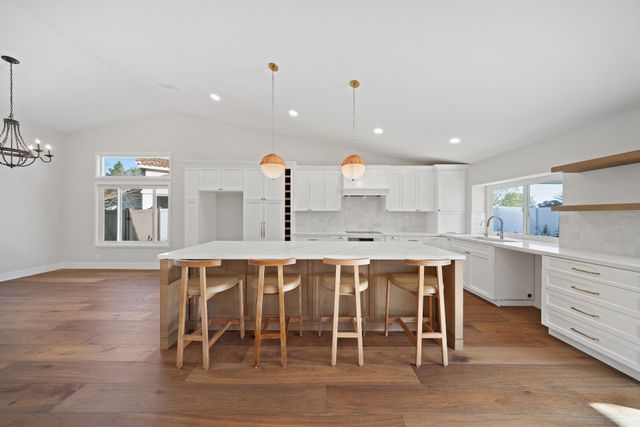 Bright modern kitchen with white cabinets, large island, wooden stools, and pendant lights
