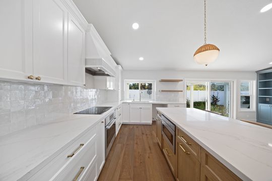 Bright modern white kitchen with wood island, recessed lights, and large windows overlooking a patio