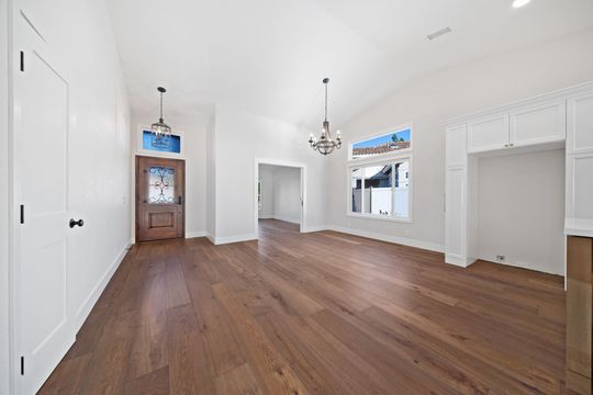 Empty white room with hardwood floors, chandelier, fireplace mantel, and built-in cabinets