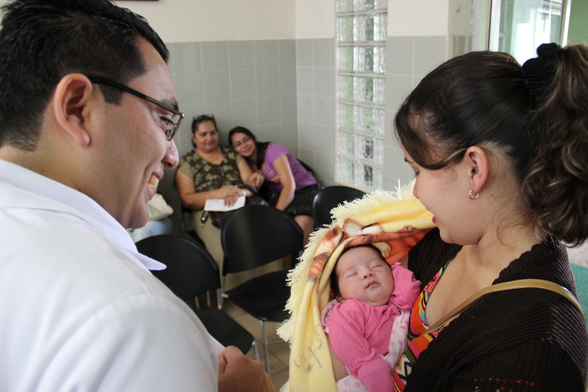 A woman is holding a baby in her arms while a man looks on.