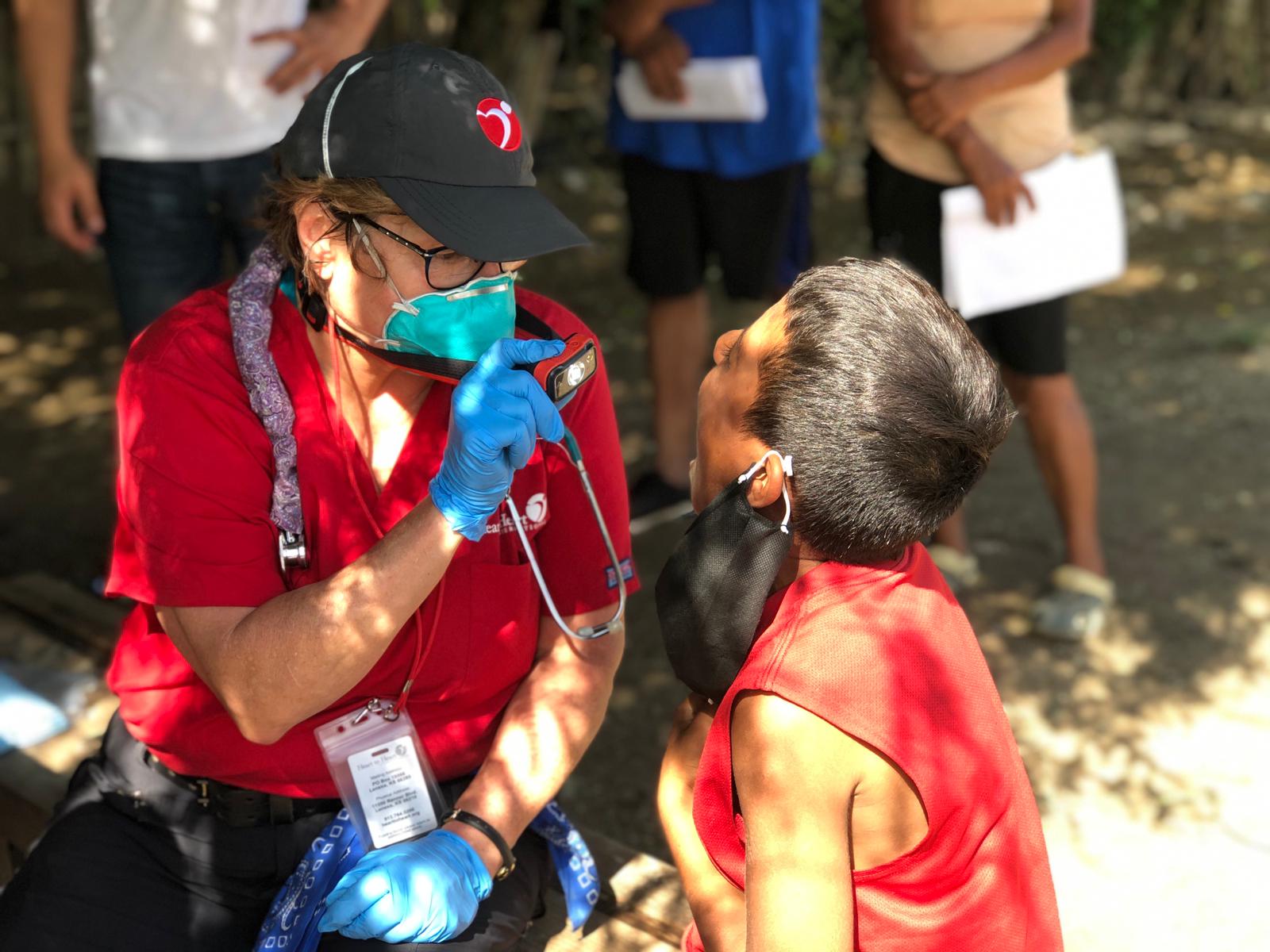A woman in a red shirt is examining a child 's teeth with a stethoscope.
