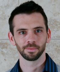 A man wearing glasses and a blue shirt is smiling for the camera.