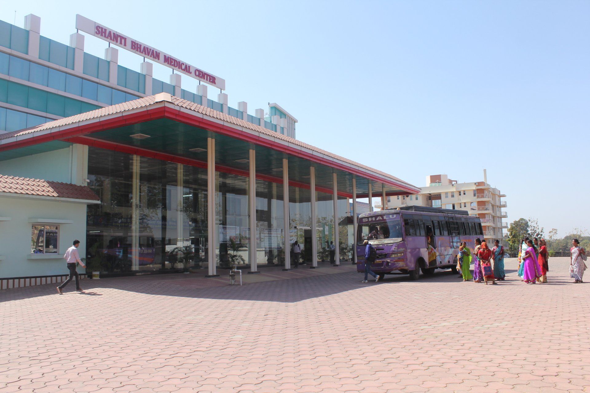 A group of people are standing outside of a building with a bus parked in front of it.