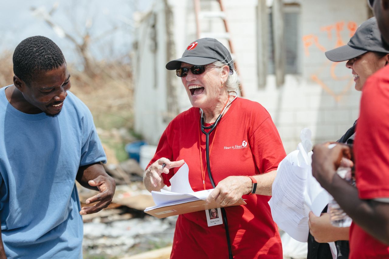A group of people are standing around a woman in a red shirt with a stethoscope around her neck.