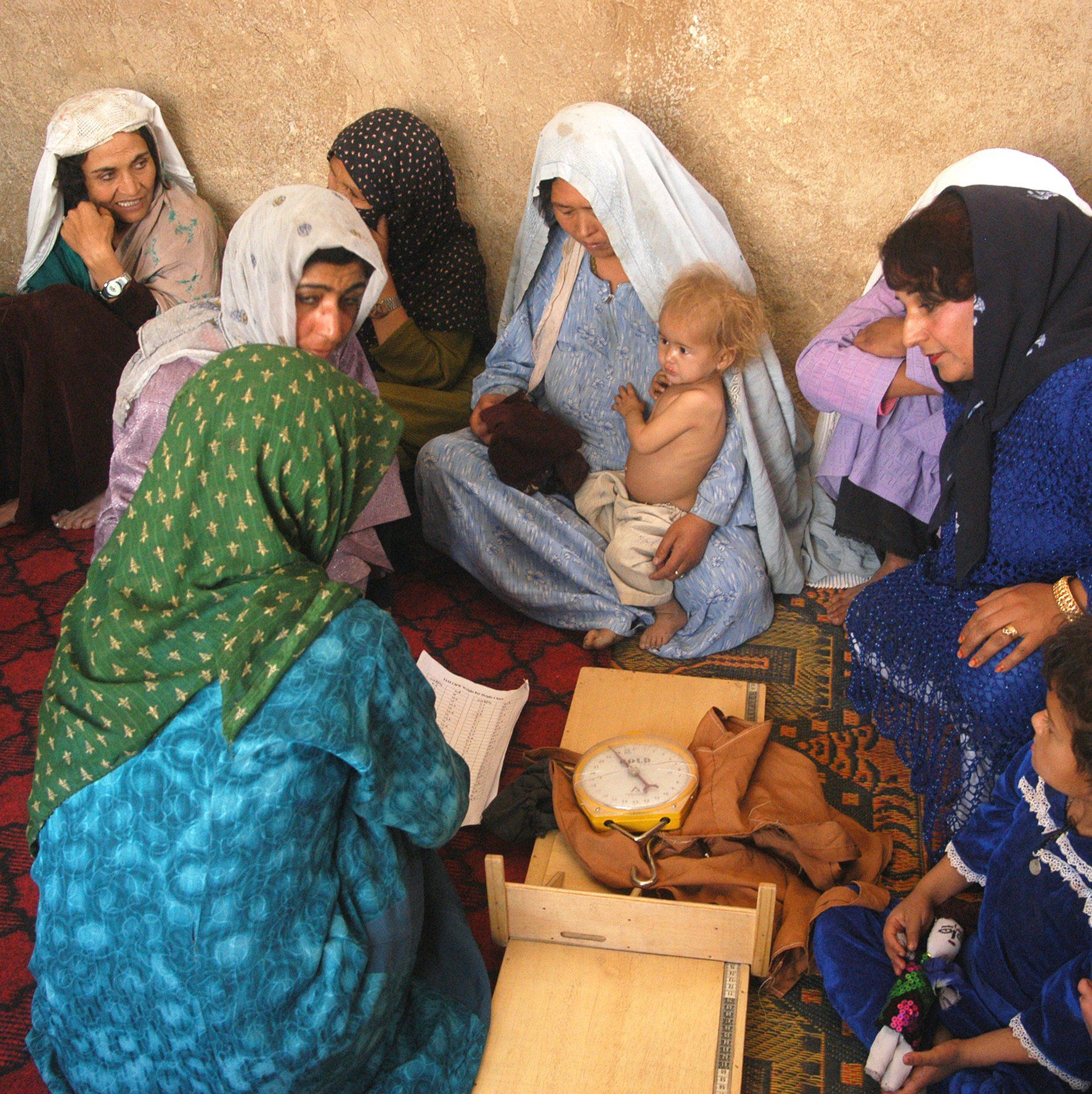 A group of women are sitting on the floor with a baby and a drum