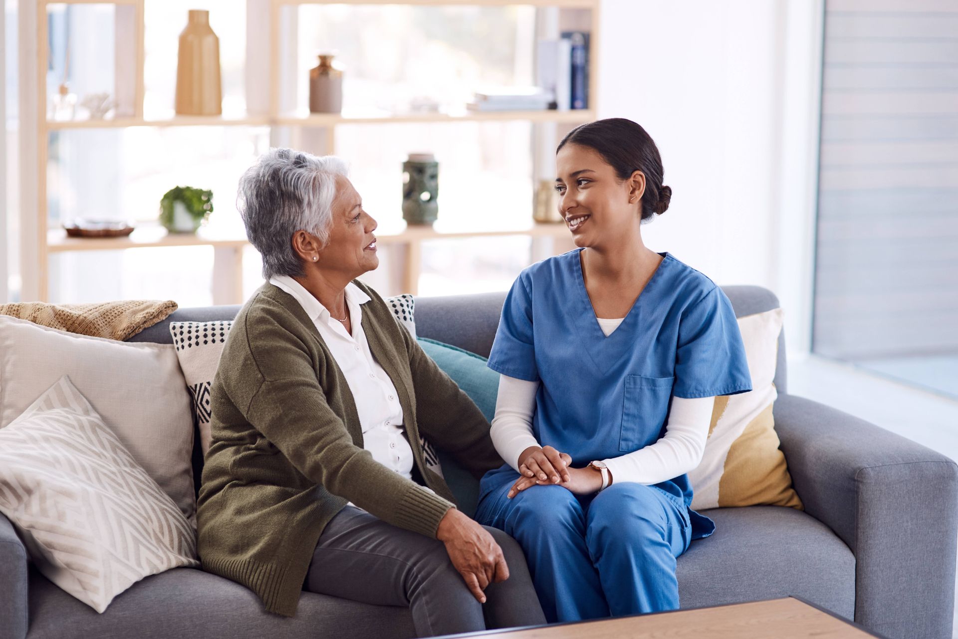 A nurse is sitting on a couch with an elderly woman.