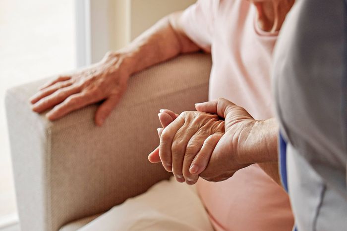 An elderly woman is sitting on a couch holding a nurse 's hand.