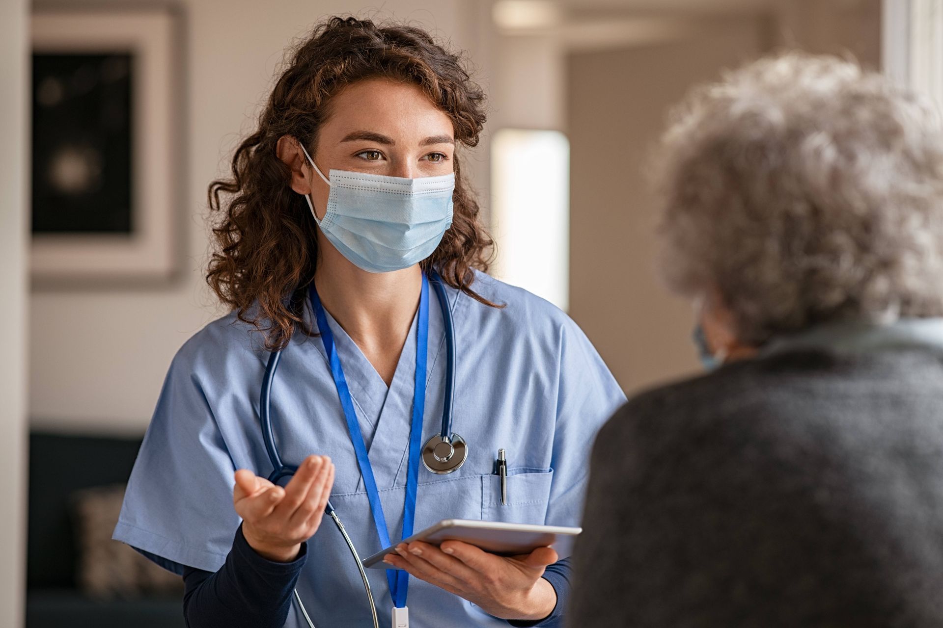 A nurse wearing a mask is talking to an elderly woman.