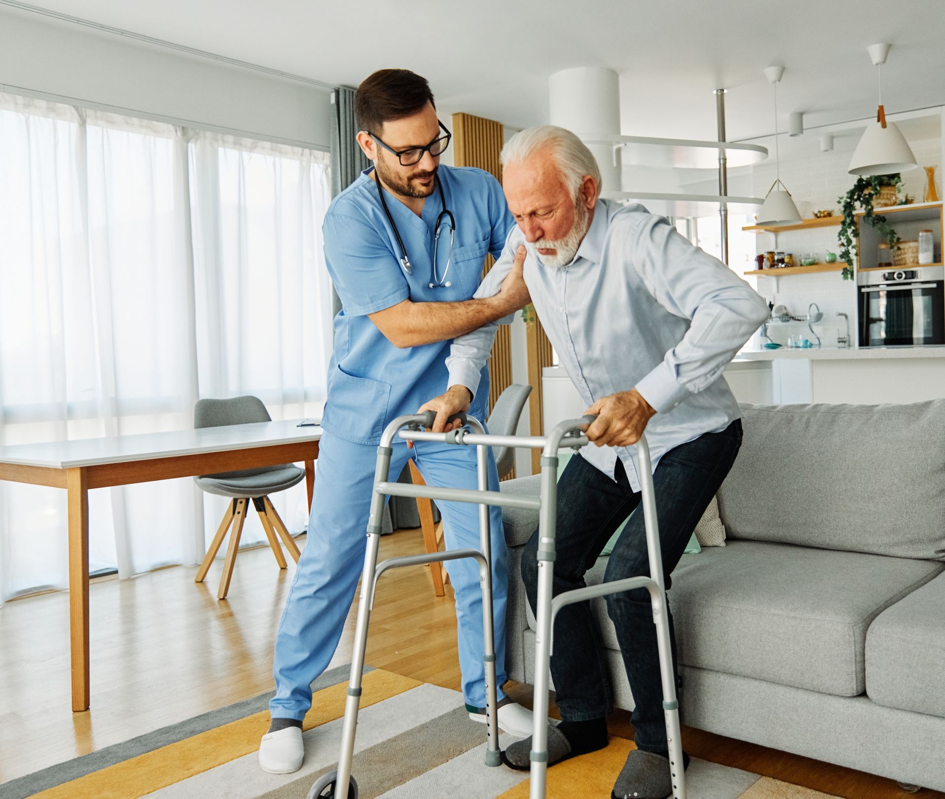 Caregiver assists an older adult using a walker. Both are in a home setting.
