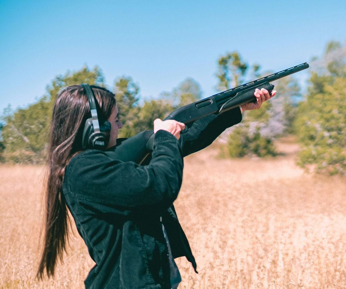 woman firing a shotgun in a field