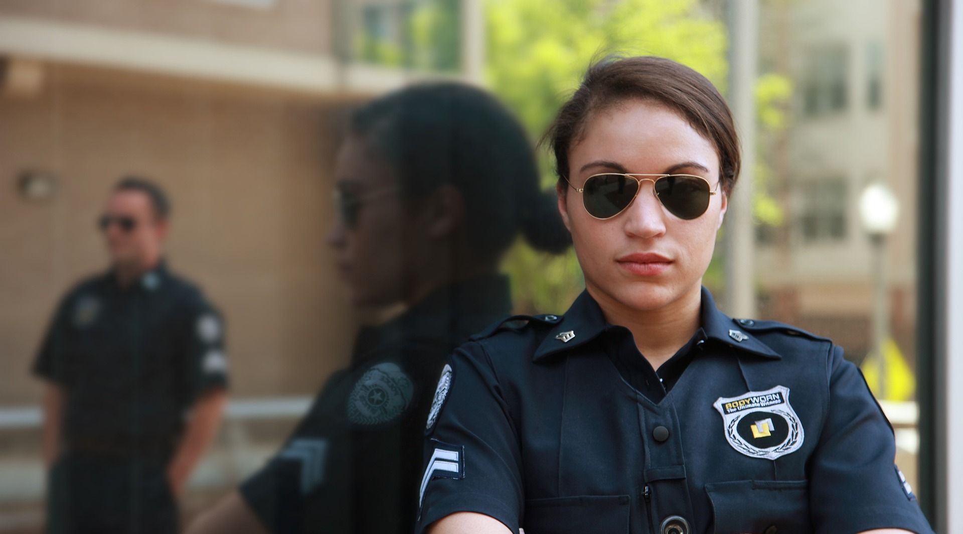 A woman in a police uniform and sunglasses is standing in front of a building.