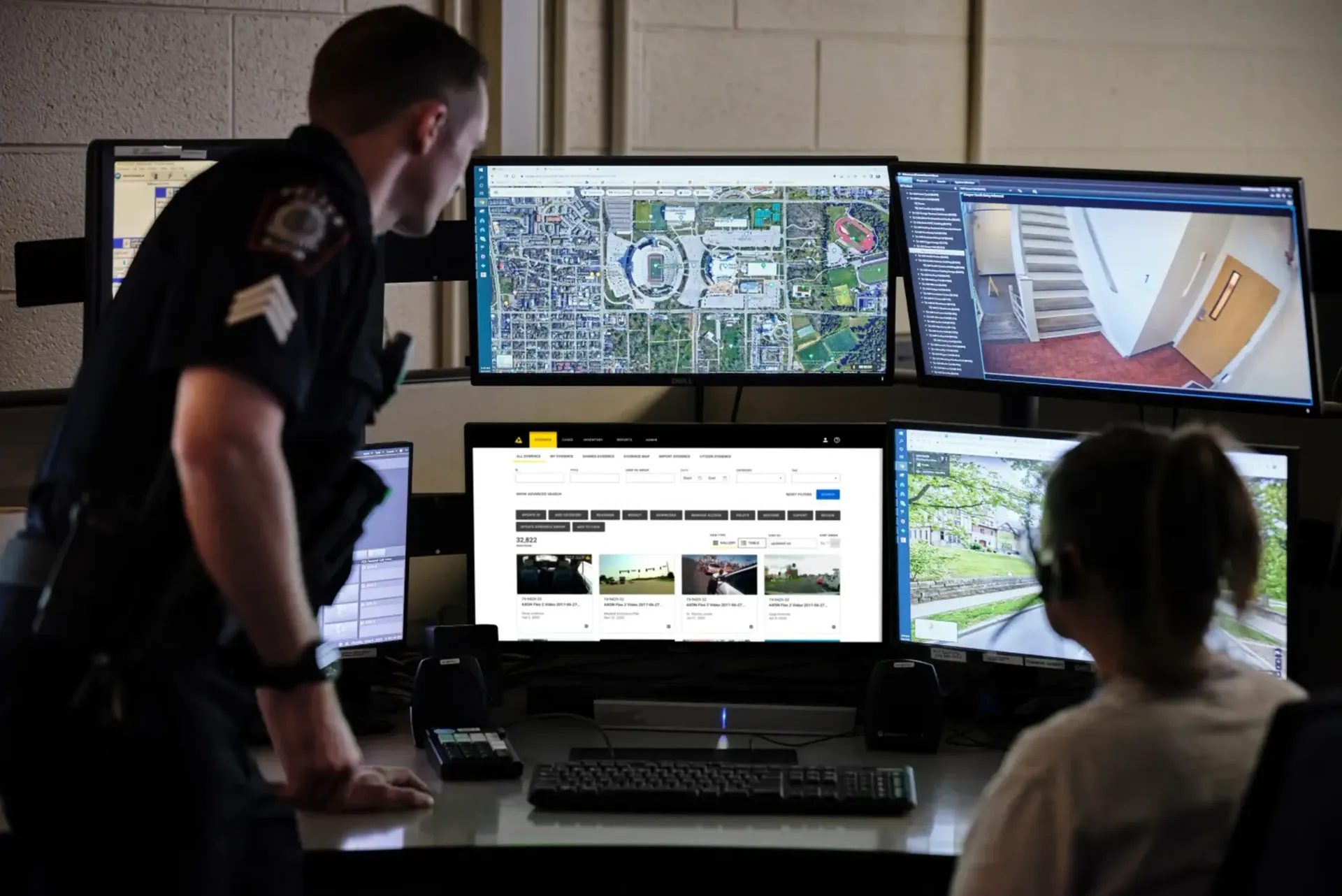 A police officer is standing next to a woman sitting in front of a computer monitor.