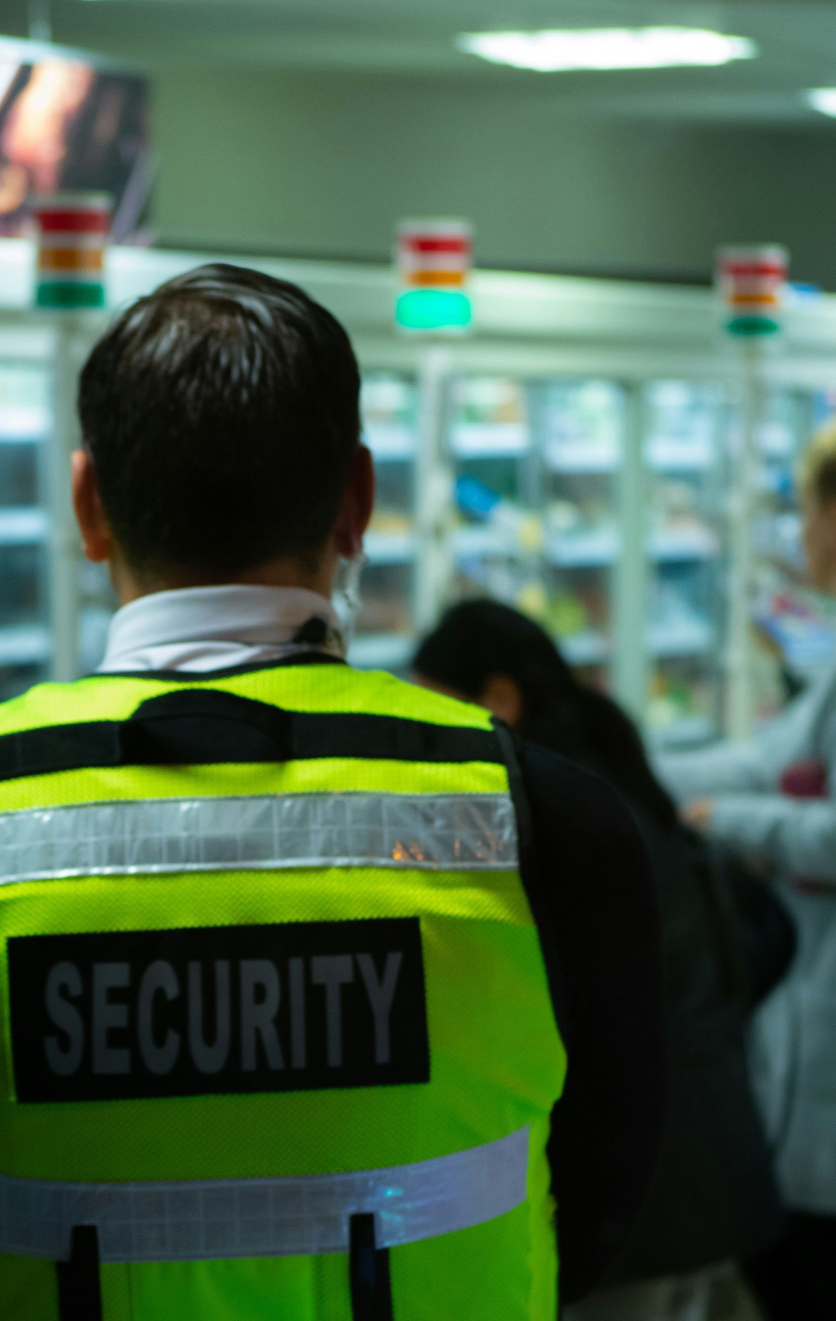 A security guard is standing in front of a crowd of people in a supermarket.