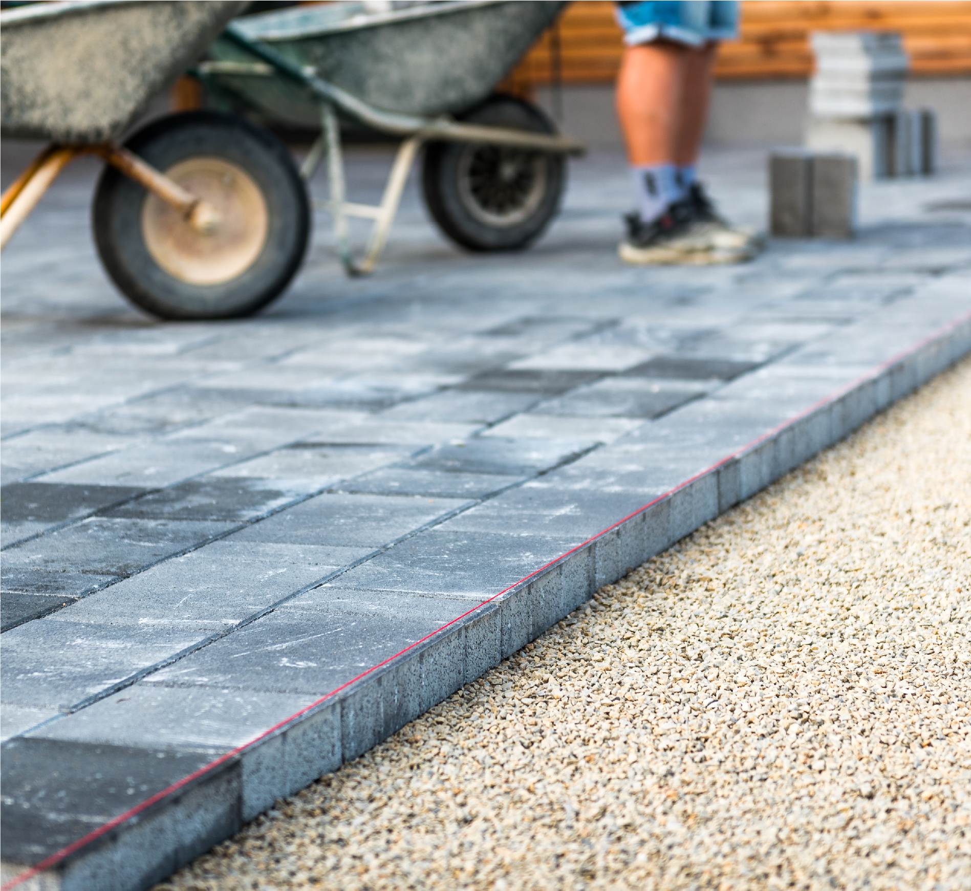 A man is pushing a wheelbarrow on a brick sidewalk.