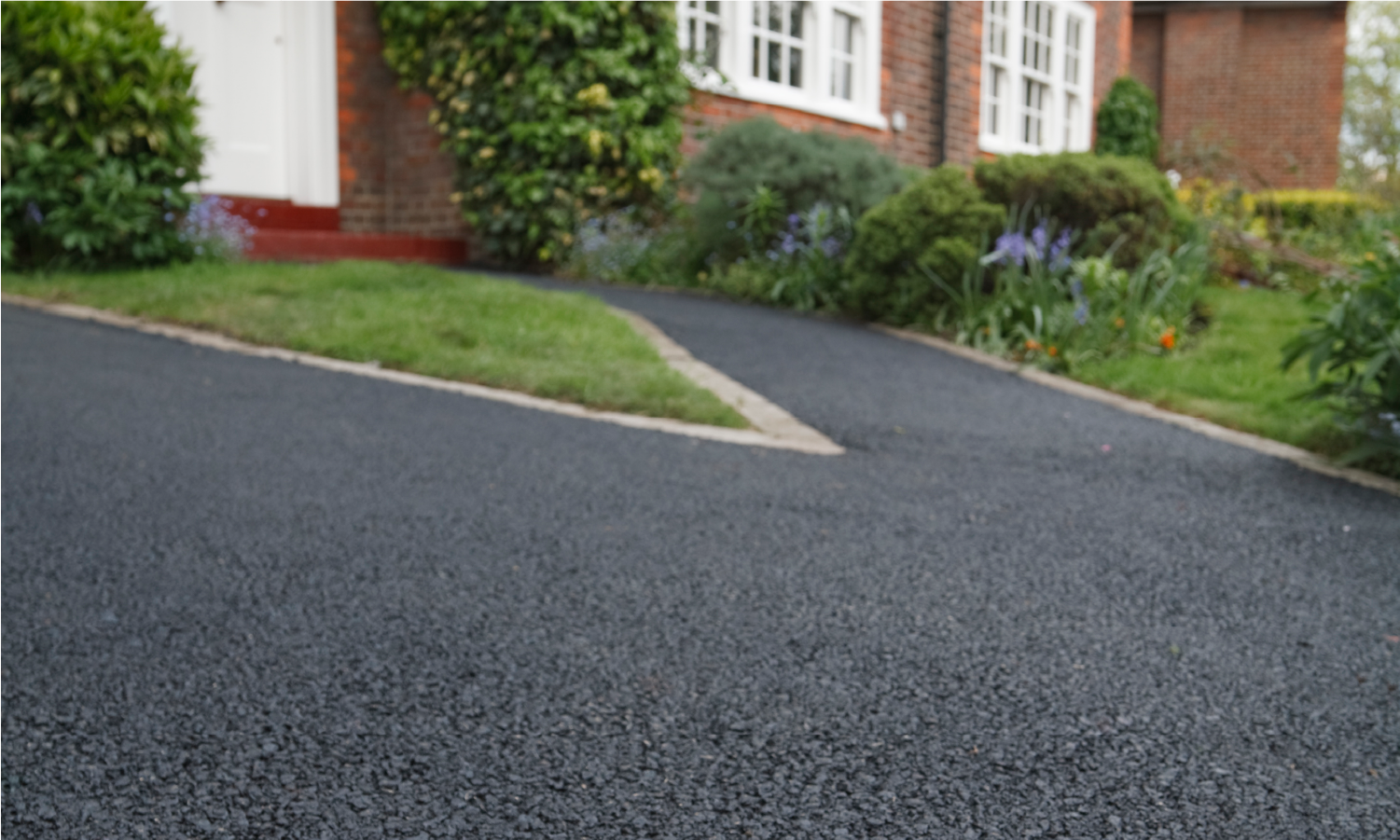 A black asphalt driveway leading to a brick house.