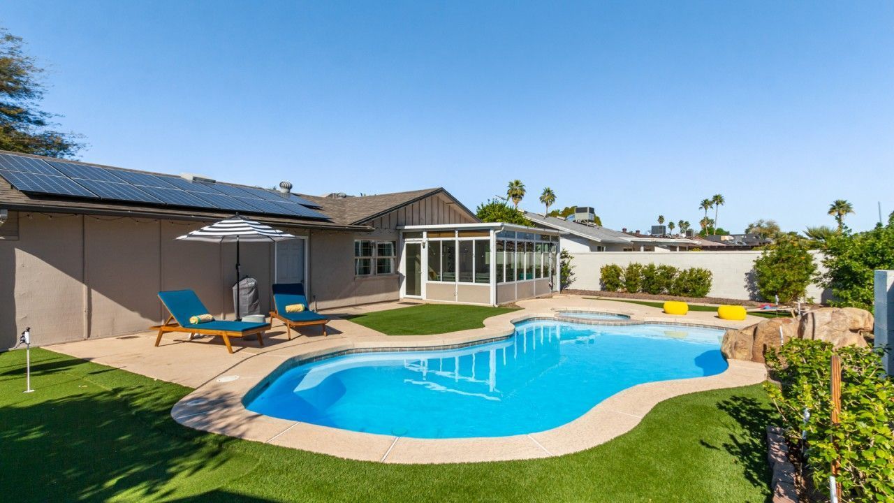 Backyard pool with patio, lawn, and a house under a clear blue sky