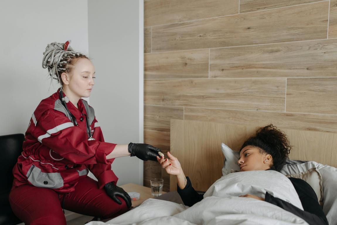 Medical professional in red uniform giving a patient in bed a pill.