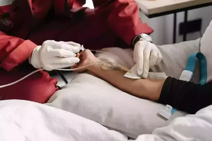 Person receiving intravenous fluids in arm; medical setting.