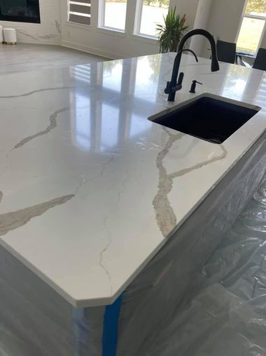White quartz kitchen island with black sink and faucet, protected with blue tape during installation