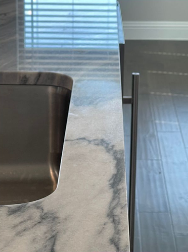 Marble kitchen island with sink next to a window and hardwood floor