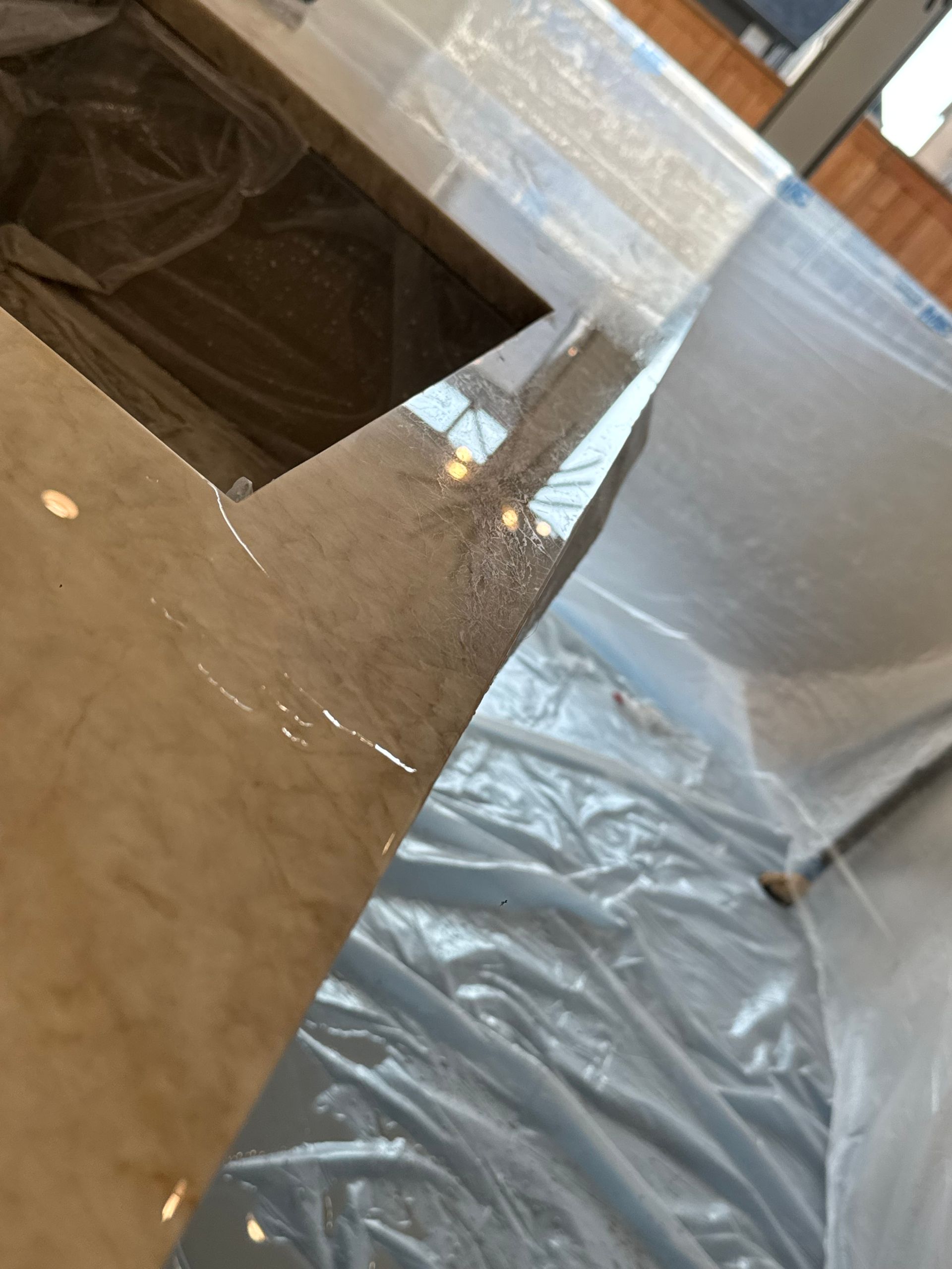 Close-up of a glossy countertop with a rectangular cutout, covered floor, and sunlight through a window.