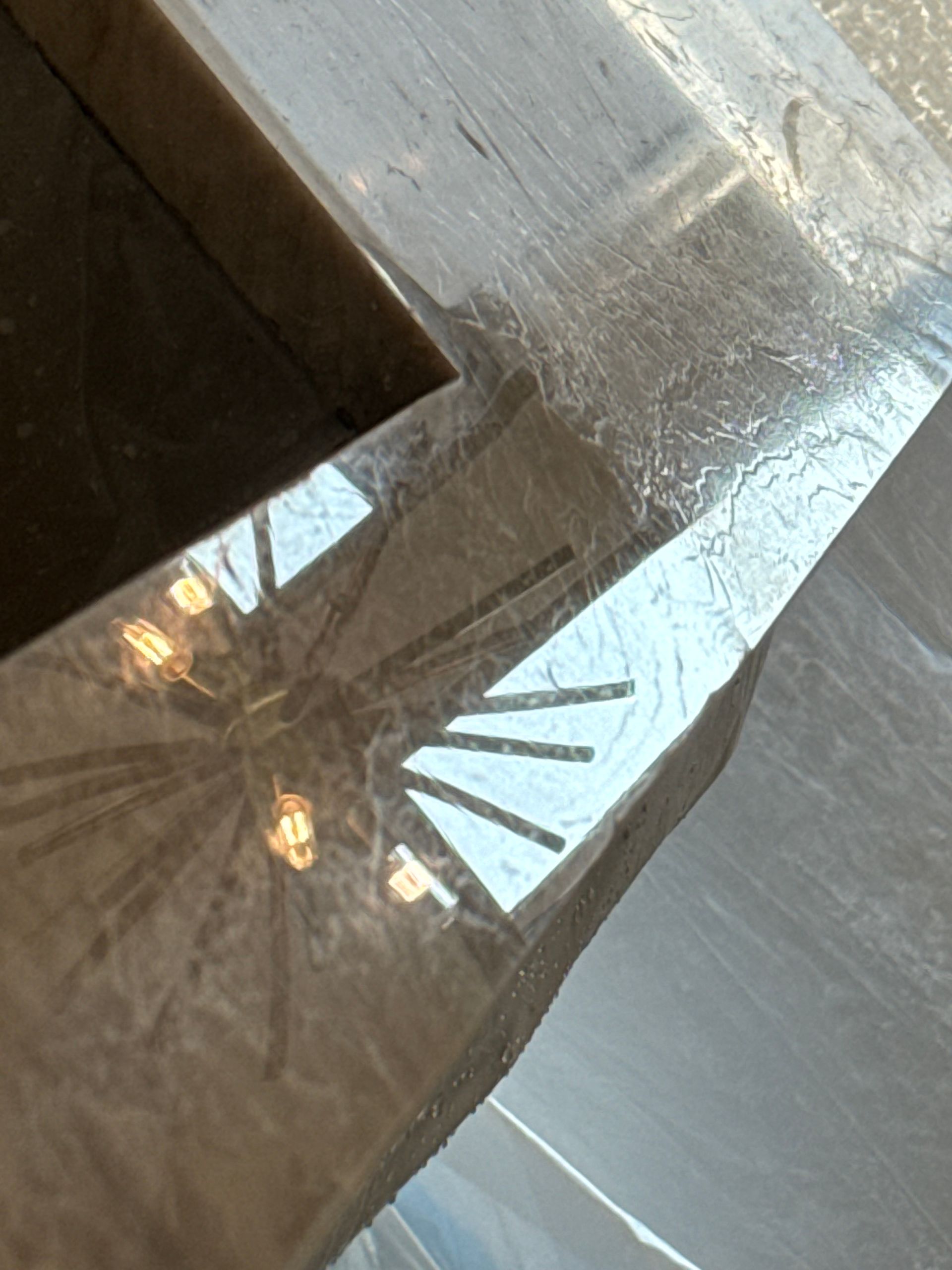 Close-up of a metallic surface reflecting a window and hanging lights inside a room