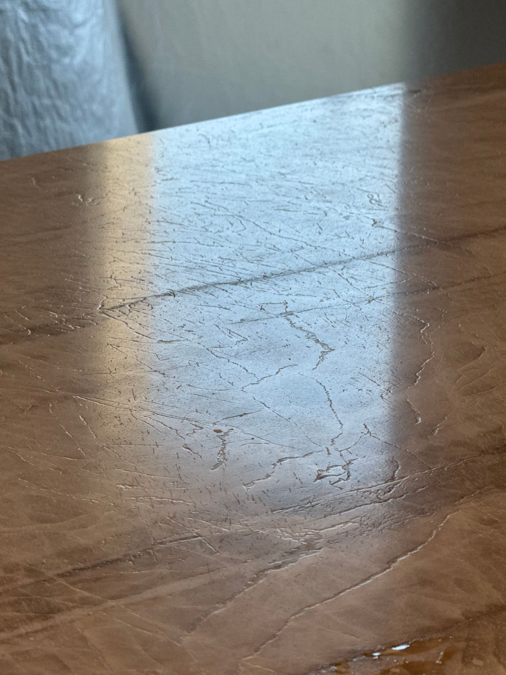 Close-up of a scratched wooden tabletop with a bright reflection on the surface