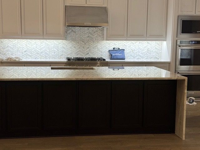 Modern kitchen with beige cabinets, stone backsplash, large island, and built-in stainless steel appliances.