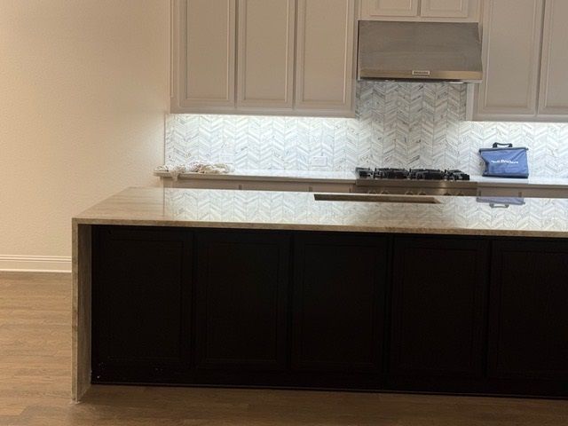Modern kitchen with black island, light cabinets, granite countertop, and stovetop with a blue dish towel.