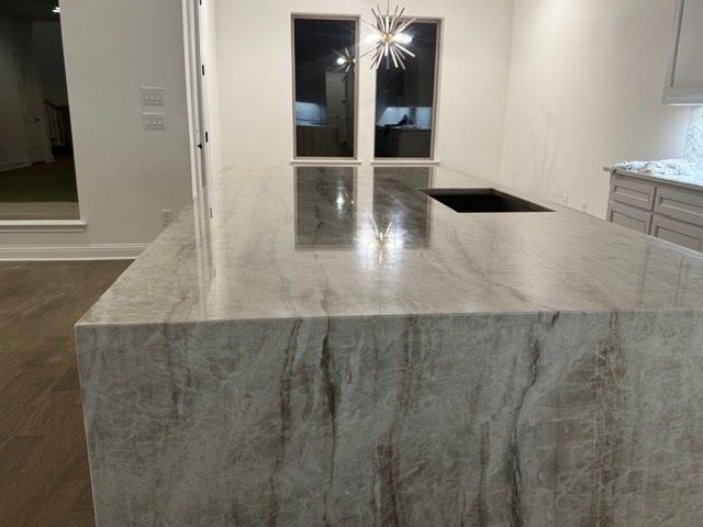 Kitchen island with polished marble countertop and a black sink in a modern, bright interior