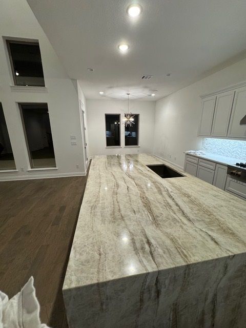 Modern kitchen with large marble island, white cabinets, wood floor, and recessed ceiling lights