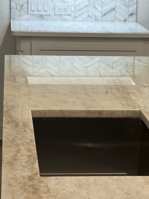 Stone kitchen island with a rectangular black sink cutout and white chevron tile backsplash behind it