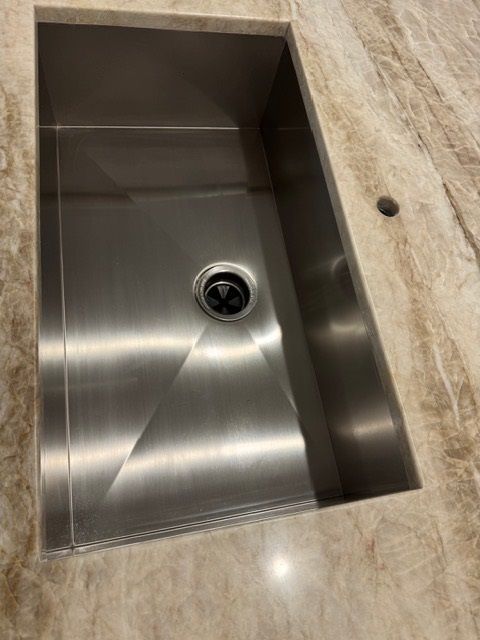 Stainless steel kitchen sink inset in a beige stone countertop, viewed from above.