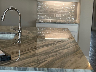 Modern kitchen with marble countertop, chrome faucet, and white cabinets behind protective plastic wrap