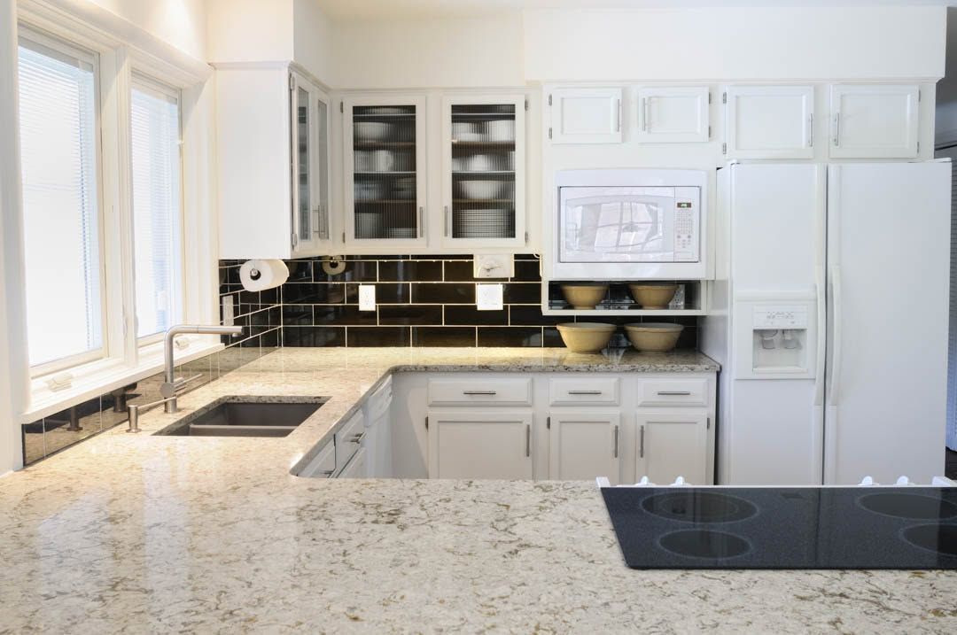 Bright white kitchen with granite countertops, black backsplash, and stainless steel appliances.