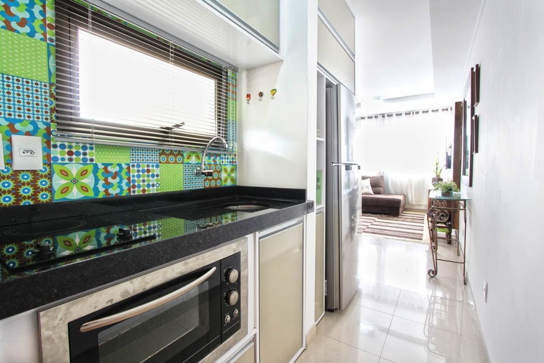 Bright kitchen with black countertop, colorful tile backsplash, and hallway leading to a sunlit living room