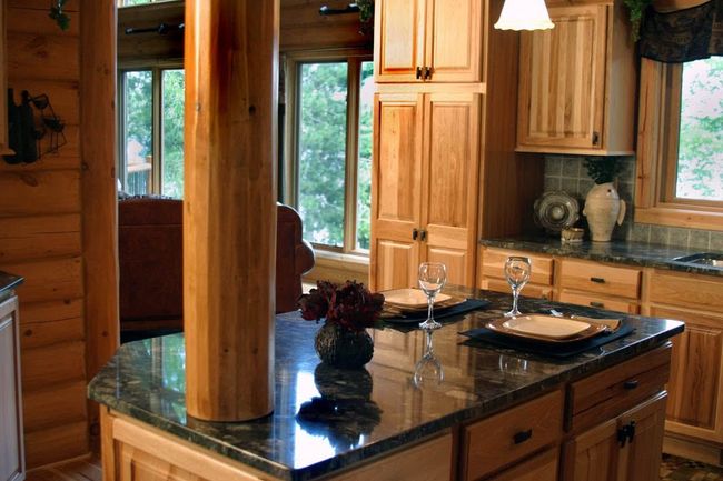 Modern log cabin kitchen with wood cabinets, black granite island, and a window overlooking trees