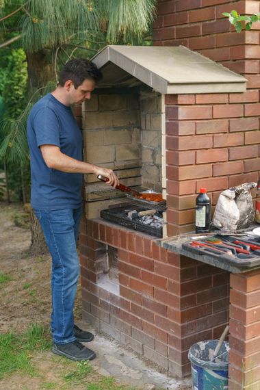 Person grilling food at an outdoor brick barbecue in a backyard