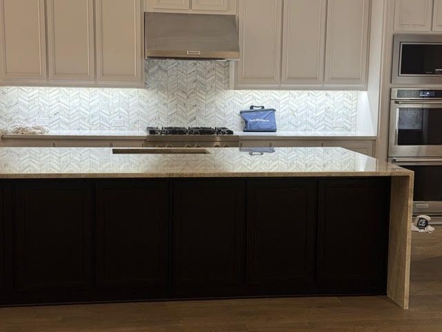 Modern kitchen with light cabinets, stainless hood, large island, and under-cabinet lighting