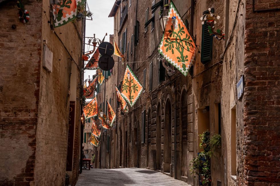 A narrow alleyway lined with brick buildings and flags hanging from the buildings.