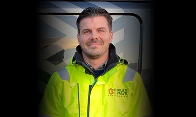 A man wearing a hard hat and safety glasses is working on a pipe.
